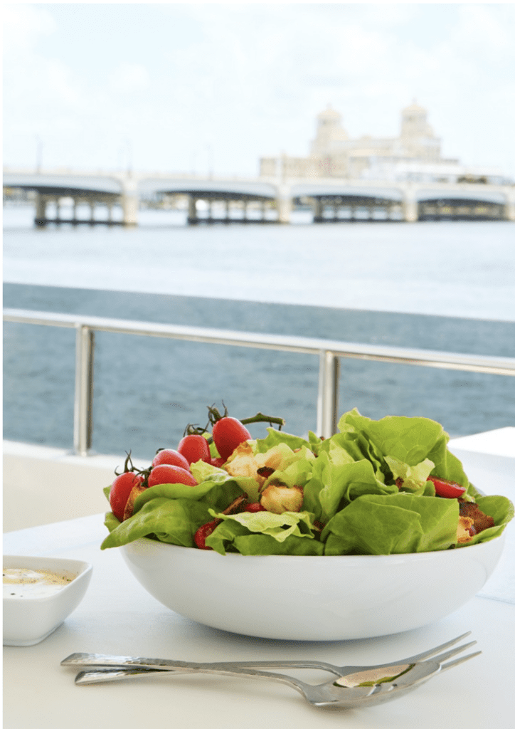 A bowl of salad on a table next to a body of water.