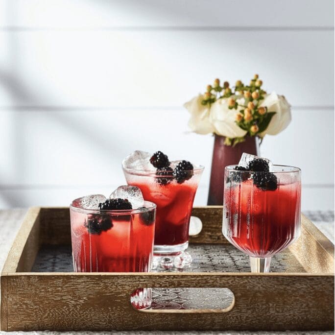 Three blackberry cocktails on a wooden tray.