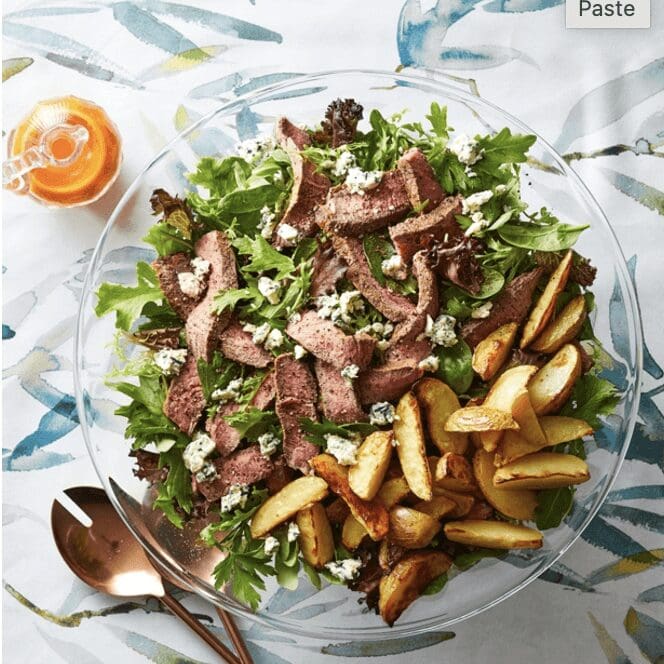 A salad with steak and potatoes on a plate.