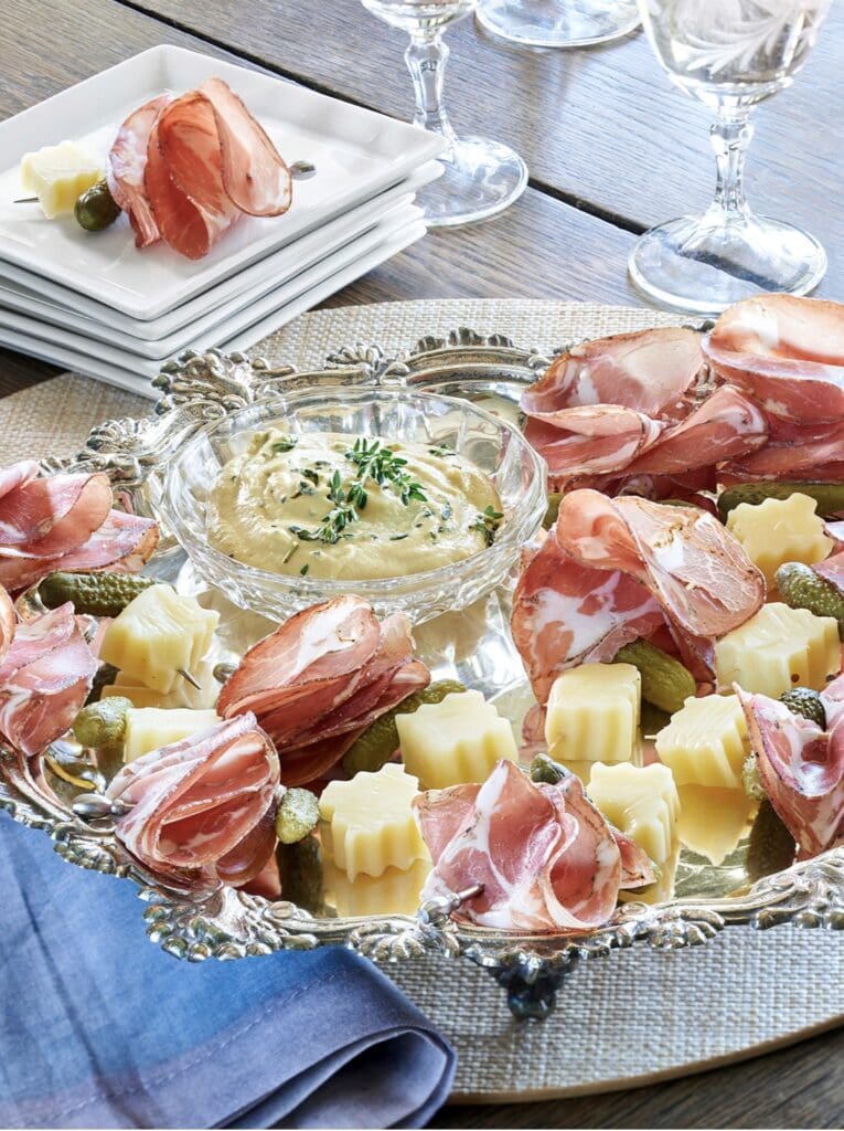 A platter of ham, cheese and pickles on a table.