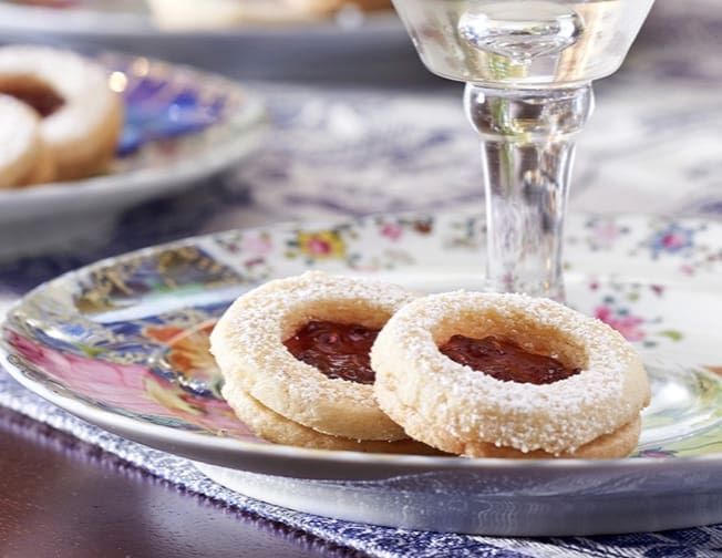 Two cookies with jam on a plate with a glass of wine.