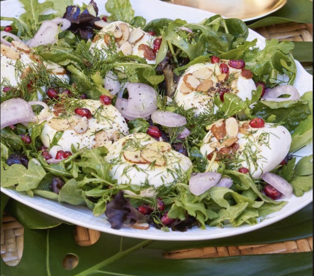 A plate with eggs, greens and pomegranate on it.