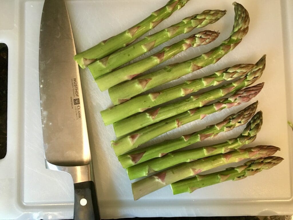 Knife with green stems on a white cutting board