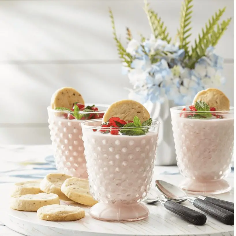 A glass of yogurt and cookies on a table.