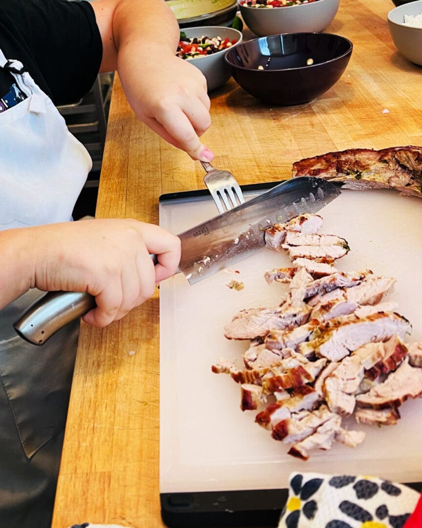 A person cutting cooked chicken on a cutting board