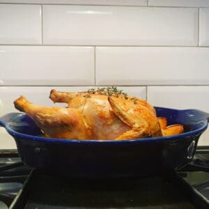 A chicken in a blue dish on top of a stove.