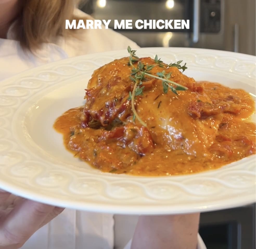 Creamy chicken dish garnished with herbs on a white plate.