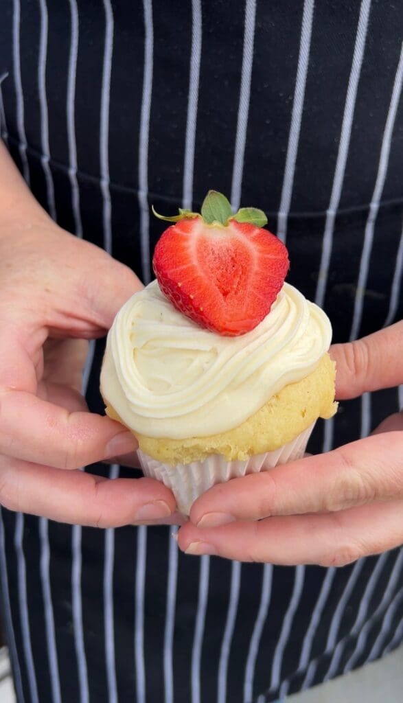 Cupcake topped with creamy frosting and a fresh strawberry half.