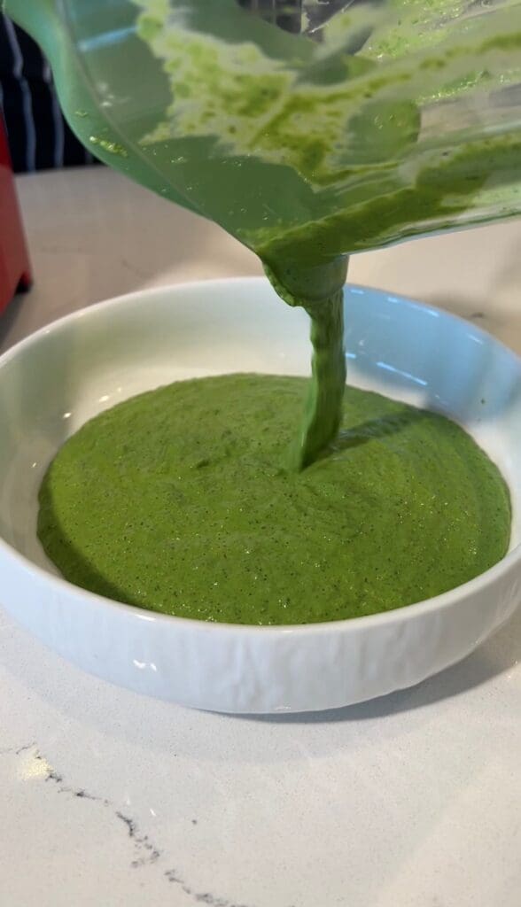 Green sauce being poured into a white bowl.