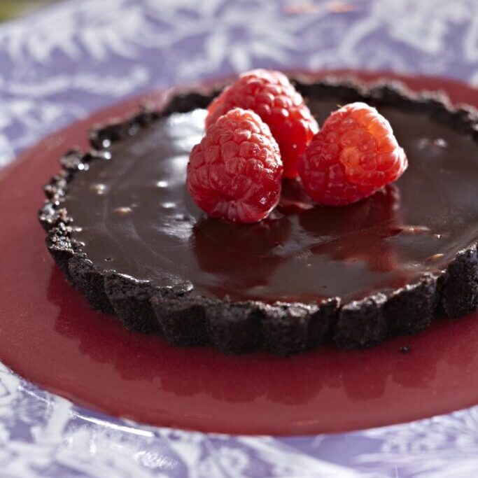 A chocolate tart with raspberries on a plate.