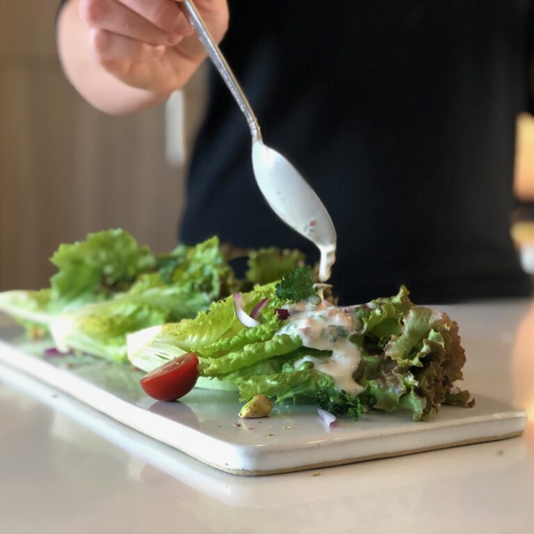 a person putting dressing on Mixed greens with tomatoes, red onion, and pistachios