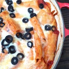 A dish of baked pasta with black olives and cheese in a red pan.