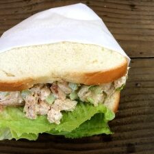 On a wooden table, there is a delicious chicken salad sandwich.