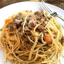 A plate of spaghetti with beef and vegetables on a wooden table, inspired by a bolognese recipe.