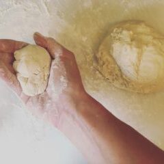 A person's hand is holding a ball of dough for a basic pizza recipe.