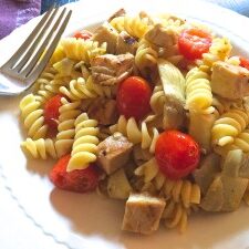 A plate of pasta with chicken and tomatoes on it.