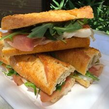 A sandwich with ham and arugula on a white plate.