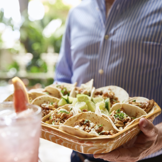 A man holding a tray of tacos and a drink.