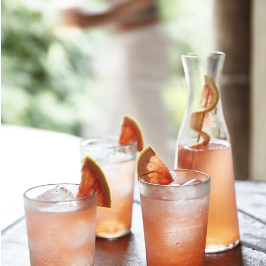 Three glasses of grapefruit infused gin and tonic on a wooden table.
