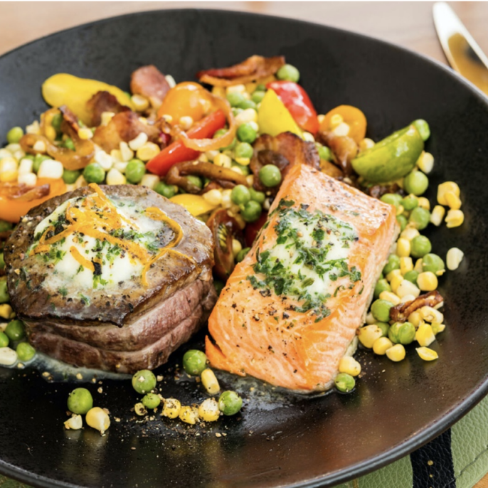 A black plate with salmon and vegetables on it.