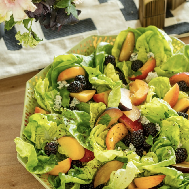 A salad with peaches and blackberries on a wooden table.
