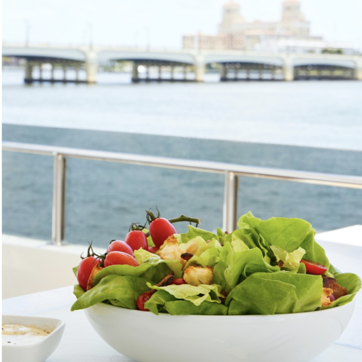 A bowl of salad on a table next to a body of water.