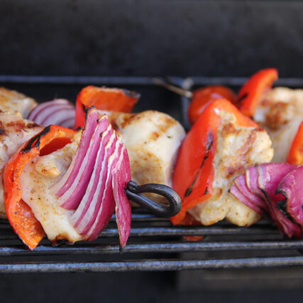 Chicken skewers with peppers and onions on a grill.