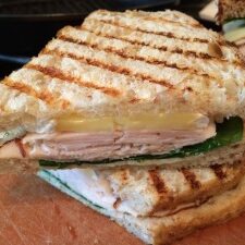 A grilled turkey sandwich with brie on a cutting board.
