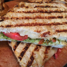 Two grilled sandwiches, one with tomato, on a wooden cutting board.